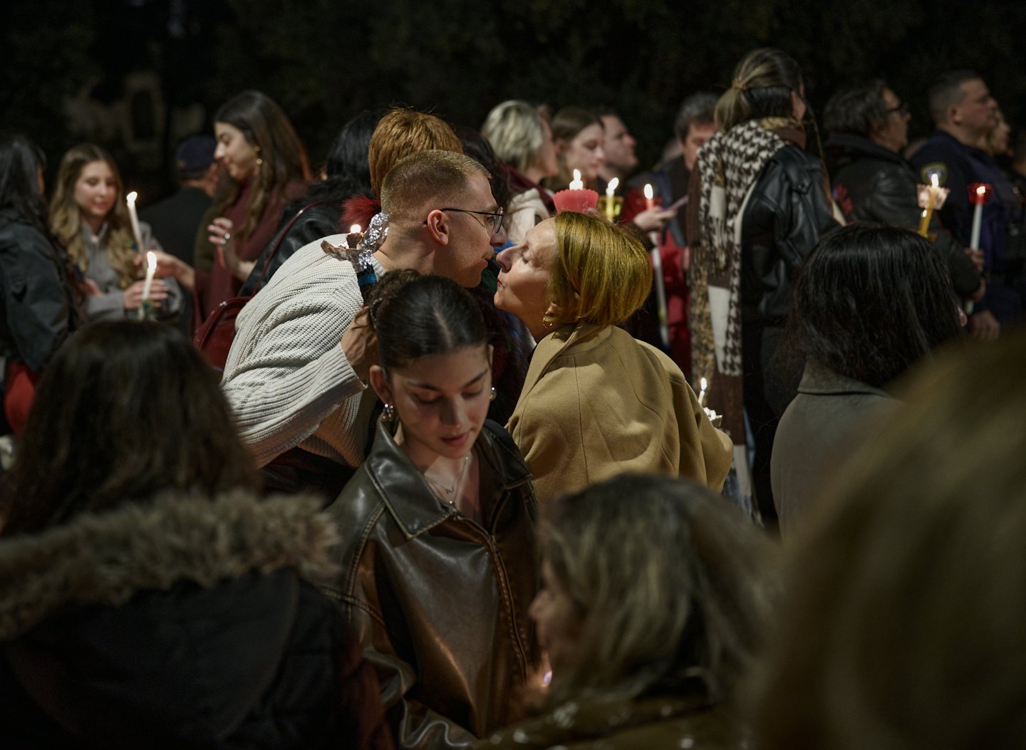 A group of people holding candles together outdoors at night.