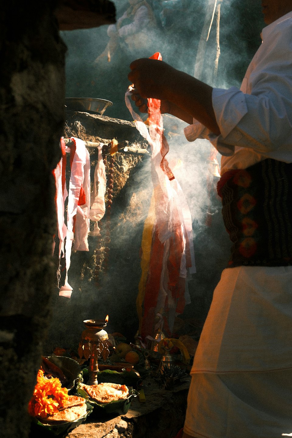 Person in white traditional clothing performs a ritual amidst smoke.