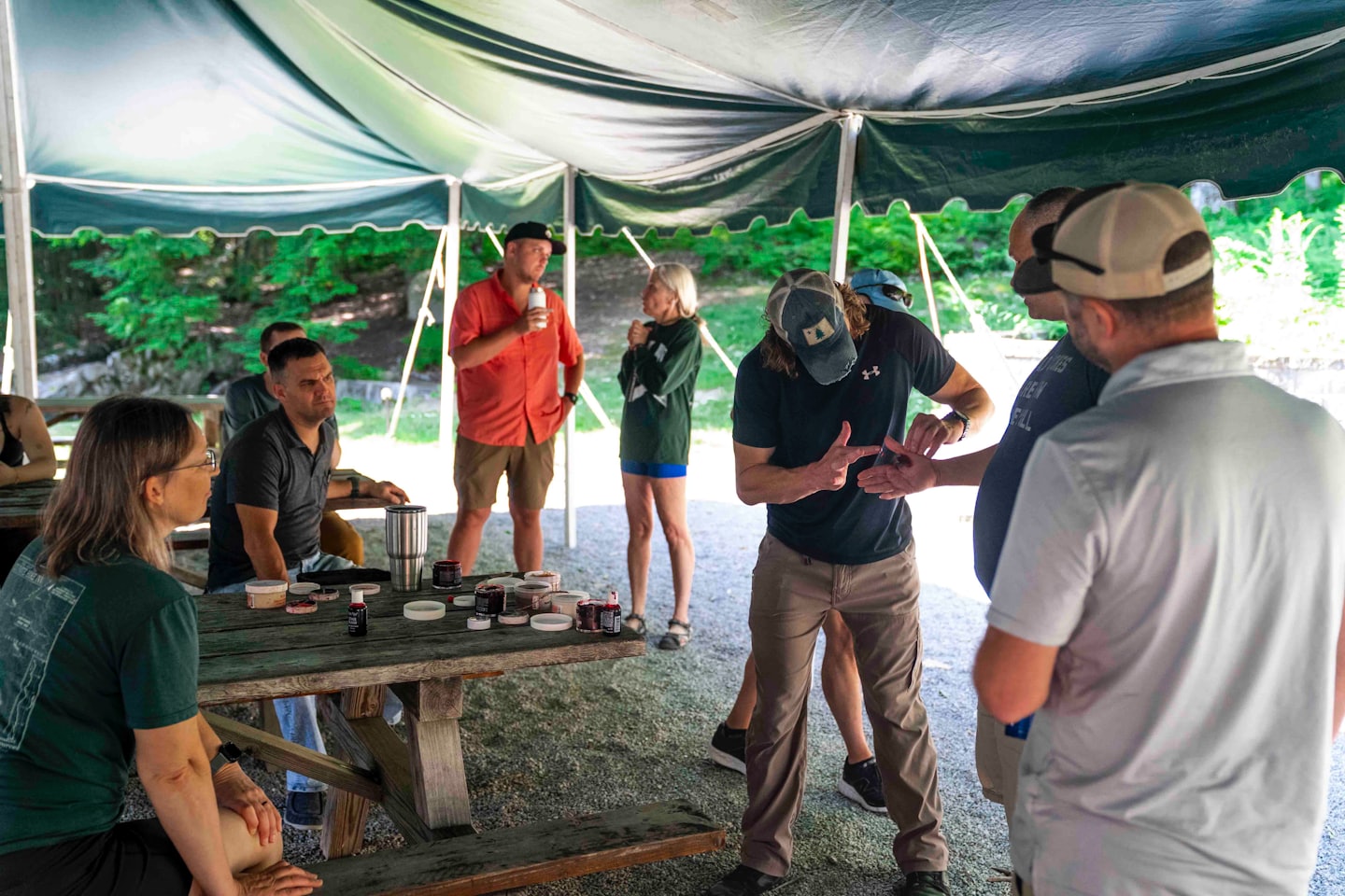 A group of adults listens to a workshop leader under a tent.